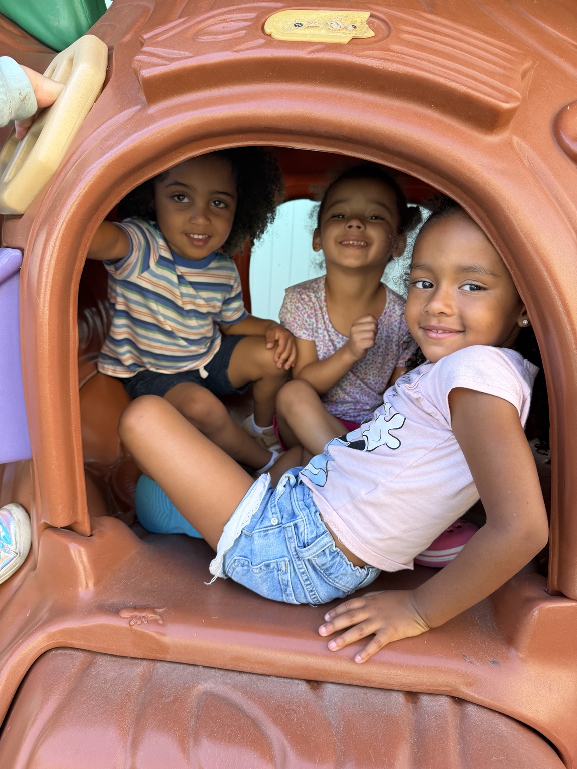Three Sunshine children smiling together in a playground tunnel